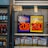 An advertisement display in a store window features lottery jackpot amounts for Mega Millions and Powerball, both showing jackpots of 208 million and 200 million respectively. Below the display, several lottery tickets and promotional posters are visible. To the left of the display, there is a refrigerator stocked with various drinks including different flavors of sports drinks and bottled water.